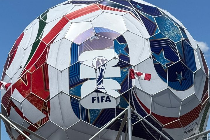 Large soccer ball sculpture near waterfront and city buildings.