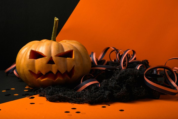 Carved pumpkin with streamers and confetti on orange and black background.