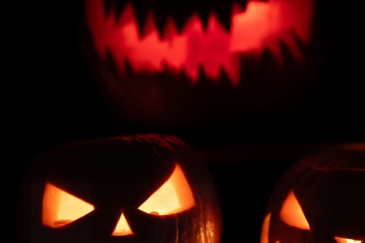 Three glowing carved pumpkins with spooky faces in the dark.