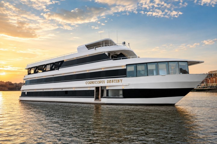 Large yacht with black and white design on calm water at sunset.